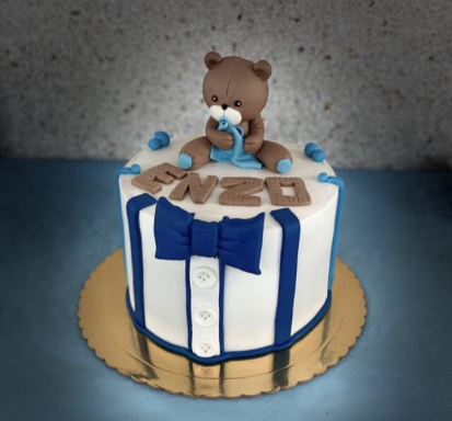 Tarta decorada con un oso de fondant y nombre "Enzo" en tonos azules y blancos.