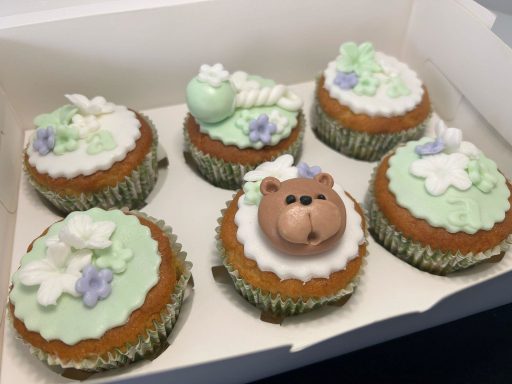 Seis cupcakes decorados con crema verde, flores y un oso de chocolate en la parte superior.