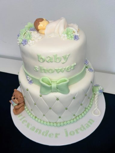 Pastel de bebé de dos pisos con un muñeco durmiendo y decoraciones en tonos verde y azul.