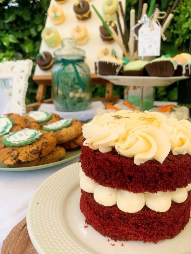 Pastel de terciopelo rojo decorado con frosting de crema, acompañado de galletas.