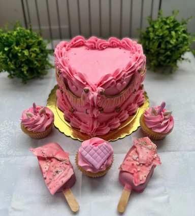 Pastel en forma de corazón rosa con cupcakes y helados decorativos alrededor.