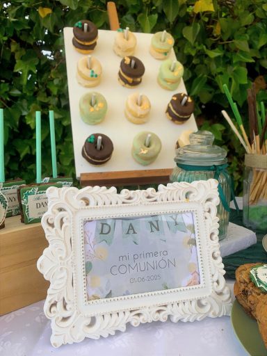 Tarta decorada con cupcakes en colores pastel y un marco blanco con un nombre.