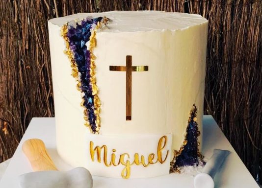 Tarta blanca decorada con una cruz y el nombre "Miguel" en dorado.