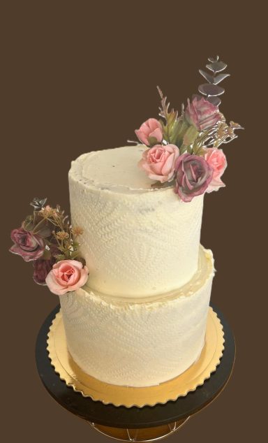 Tarta de dos pisos decorada con flores rosas y moradas en un fondo marrón.