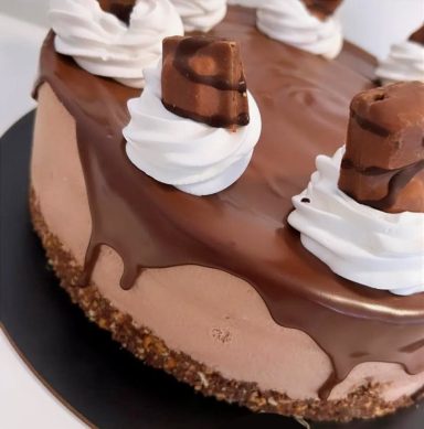 Tarta de chocolate con cobertura brillante y decoraciones de nata y trozos de chocolate.