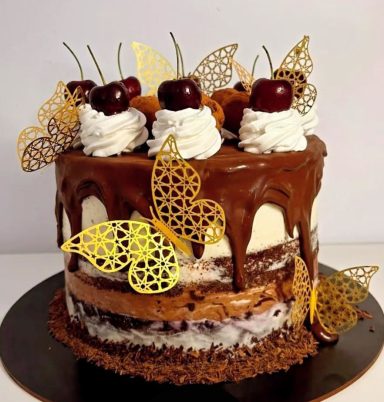 Tarta de chocolate decorada con cerezas, crema y mariposas doradas.