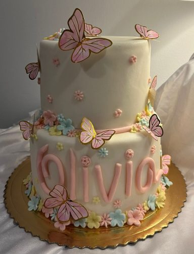 Pastel de cumpleaños de dos pisos decorado con mariposas y el nombre "Olivia".