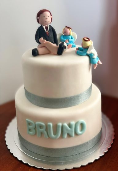 Tarta de dos pisos decorada con figuras de un hombre y dos bebés, con el nombre "BRUNO".